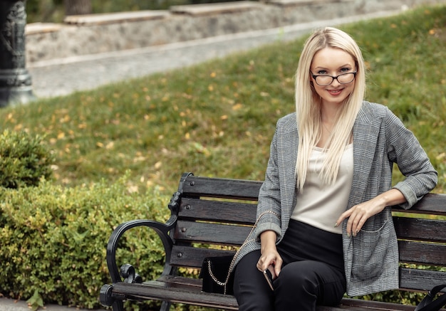 Blonde Geschäftsdame, die auf einer Bank im Park sitzt