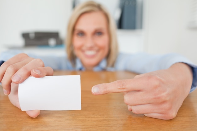 Blonde Geschäftsfrau, die auf eine Karte sich duckt hinter ihrem Schreibtisch zeigt