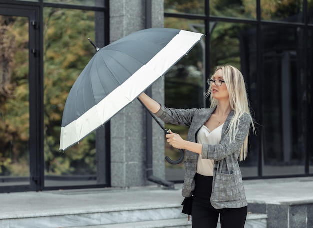 Blonde Geschäftsfrau mit Regenschirm auf dem Hintergrund eines Geschäftsbüros. Warten auf den Regen