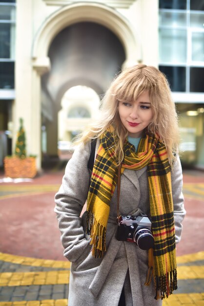 Blonde hübsche Fotografin Frau mit Retro-Kamera in ihren Händen beim Fotografieren an der städtischen alten Architektur.