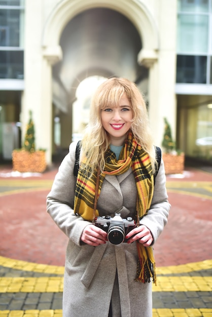 Blonde hübsche Fotografin Frau mit Retro-Kamera in ihren Händen beim Fotografieren an der städtischen alten Architektur.