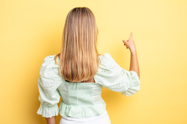 Blonde hübsche Frau, die auf dem Kopierraum steht und auf ein Objekt zeigt, Rückansicht