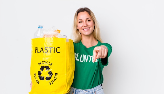 Blonde hübsche Frau, die auf die Kamera zeigt und Sie für das Recycling-Konzept auswählt