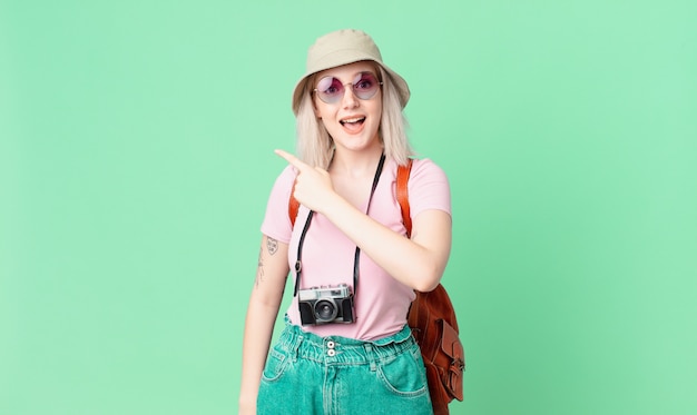 Blonde hübsche Frau, die aufgeregt und überrascht aussieht und auf die Seite zeigt. Sommerkonzept