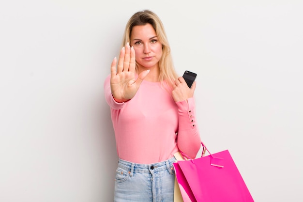 Blonde hübsche Frau, die ernsthaft aussieht und eine offene Handfläche zeigt, die eine Stoppgeste macht