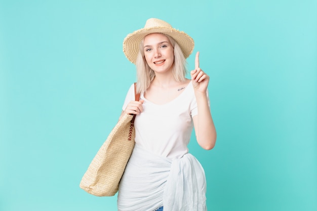 Blonde hübsche Frau, die freundlich lächelt und schaut und Nummer eins zeigt. Sommerkonzept