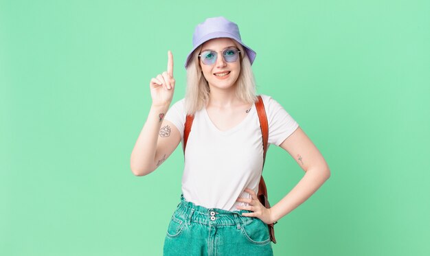 Blonde hübsche Frau, die freundlich lächelt und schaut und Nummer eins zeigt. Sommerkonzept