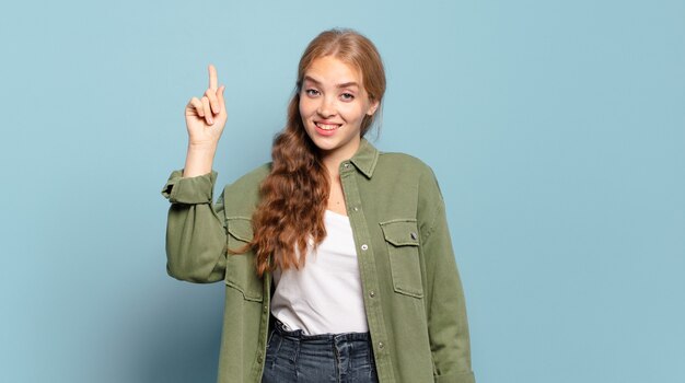 Blonde hübsche Frau, die fröhlich und glücklich lächelt und mit einer Hand nach oben zeigt, um Raum zu kopieren