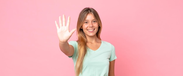 Blonde hübsche Frau, die lächelt und freundlich aussieht, die Nummer fünf oder fünf mit der Hand nach vorne zeigt und herunterzählt