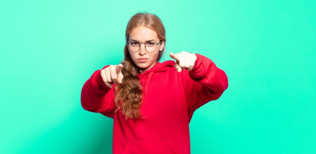 Blonde hübsche Frau, die mit beiden Fingern und wütendem Ausdruck nach vorne auf die Kamera zeigt und dir sagt, dass du deine Pflicht tun sollst