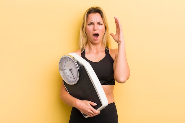 Blonde hübsche Frau, die mit den Händen in der Luft schreit