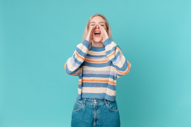 Blonde hübsche Frau, die sich glücklich fühlt und mit den Händen neben dem Mund einen großen Schrei ausstößt