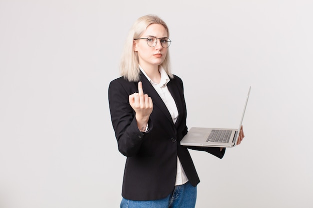 Blonde hübsche Frau, die sich wütend, verärgert, rebellisch und aggressiv fühlt und einen Laptop hält