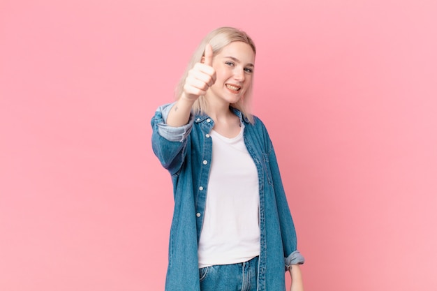 Blonde hübsche Frau, die stolz ist und positiv mit Daumen nach oben lächelt