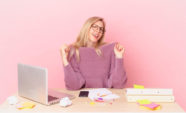 Blonde hübsche Frau junge blonde Frau, die arrogant, erfolgreich, positiv und stolz aussieht und mit einem Laptop arbeitet