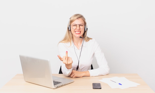 Blonde hübsche Frau junge blonde Frau, die sich wütend, verärgert, rebellisch und aggressiv fühlt und mit einem Laptop arbeitet