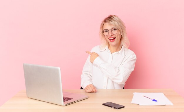 Blonde hübsche Frau junge hübsche Frau, die aufgeregt und überrascht schaut und auf die Seite zeigt. Arbeitsplatz-Schreibtisch-Konzept