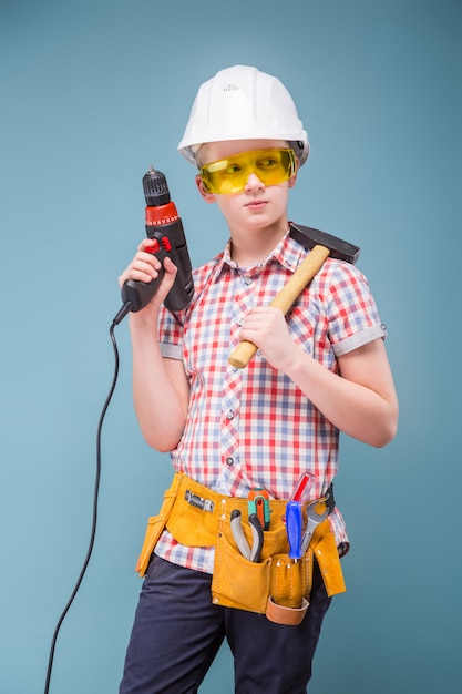 Blonde Jugendlichblondine im Bausturzhelm mit einem Schraubenzieher und einem Hammer