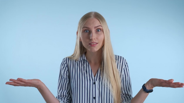 Foto blonde junge frau, die etwas auf blauem hintergrund missversteht