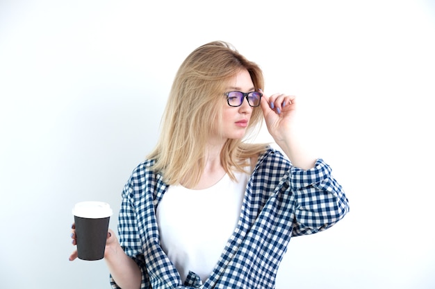 Blonde junge Frau in den Gläsern im Hemd, das schwarze Kaffeetasse hält