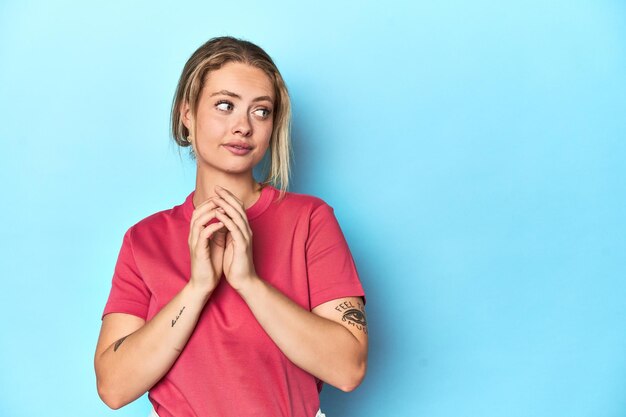 Foto blonde junge frau in rotem t-shirt auf blauem hintergrund, die einen plan im kopf hat und eine idee aufstellt