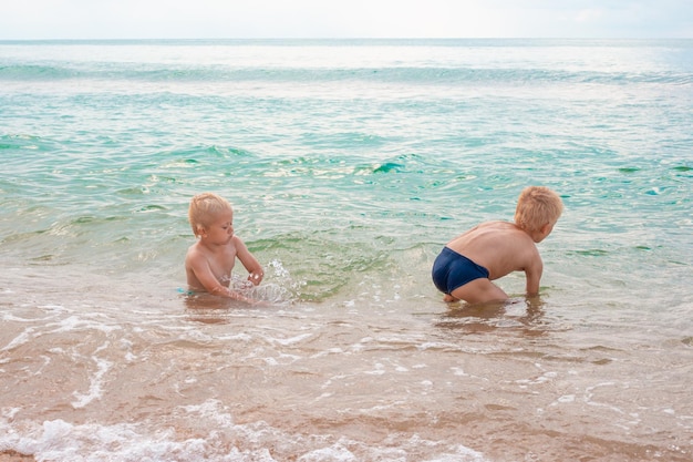 Blonde Jungenbrüder, die an einem Sommertag im Meerwasser an einem Sandstrand spielen Spaßurlaub