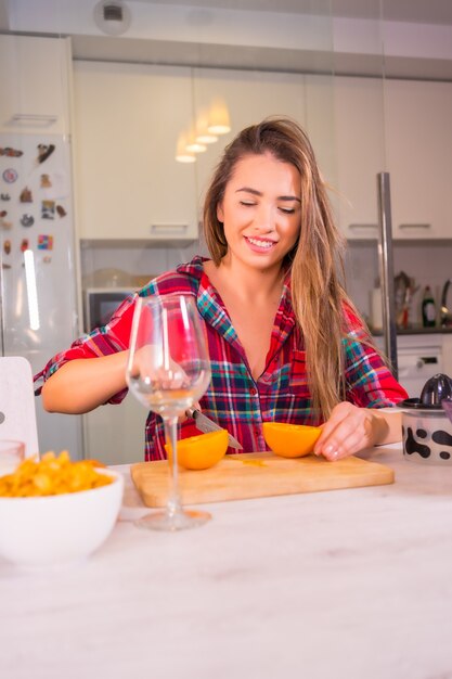 Blonde kaukasische Frau, die einen frischen Orangensaft zum Frühstück in ihrer Küche, vertikales Foto hat