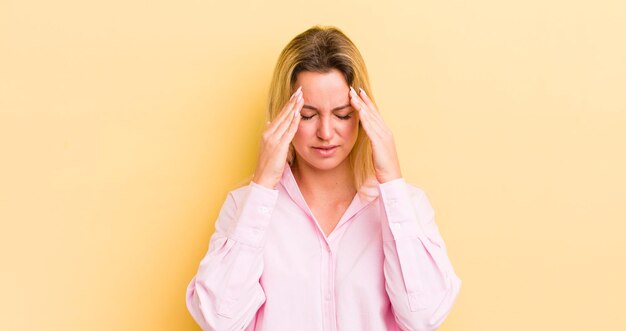 Blonde kaukasische Frau, die gestresst und frustriert aussieht, unter Druck mit Kopfschmerzen arbeitet und mit Problemen beunruhigt ist