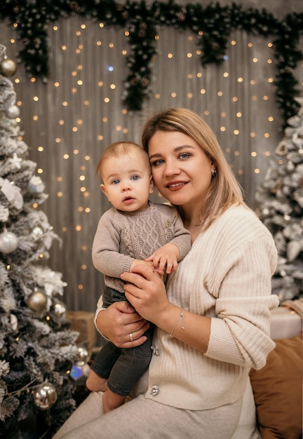 Blonde Mama sitzt auf der Couch und umarmt einen kleinen Jungen vor einem Neujahrshintergrund