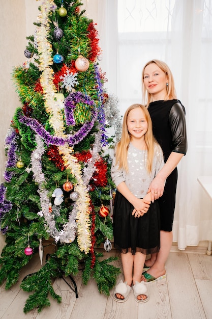 Blonde Mutter und Tochter am Weihnachtsbaum. eine glückliche alleinerziehende Mutter und eine Tradition, das neue Jahr zu Hause zu feiern. die Einstellung von Kindern und Eltern.