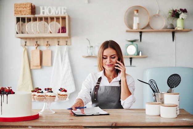 Blonde nimmt eine telefonische Bestellung entgegen. Hausgemachte Kekse und Kuchen auf dem Tisch.