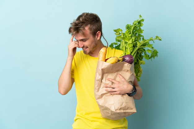 Blonde Person, die eine Tüte Essen zum Mitnehmen lokalisiert auf blauem Hintergrund lachend nimmt