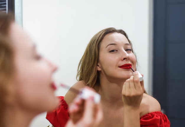 Blonde schöne Frau, die einen roten Lippenstift aufwendet und in den Spiegel schaut
