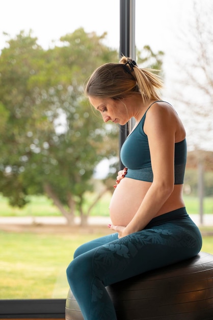 Blonde schwangere Frau praktiziert Yoga mit einem großen Ball im Wohnzimmer zu Hause