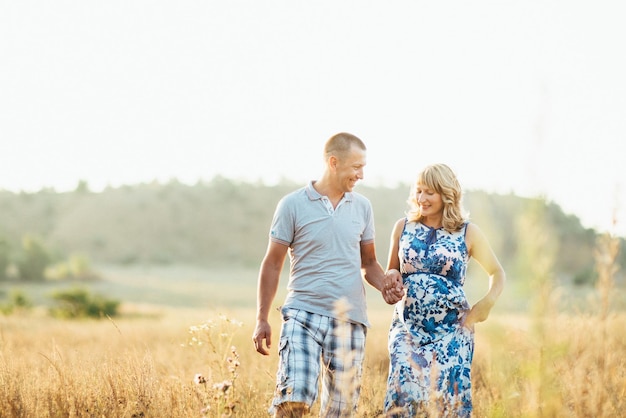 Blonde schwangere Mutter in einem blauen Kleid und ein Mann auf einem Feld