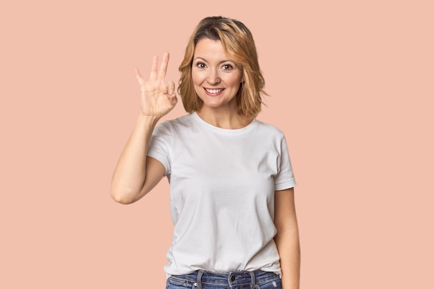 Blonde weiße Frau mittleren Alters im Studio, fröhlich und selbstbewusst und zeigt eine ok Geste.