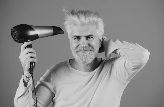 Blonder bärtiger Mann, Haare trocken, gutaussehender Mann mit langen Haaren trocknet sein Haar mit einem Haartrockner