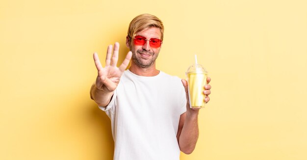 Blonder erwachsener Mann lächelt und sieht freundlich aus und zeigt Nummer vier mit einem Milchshake