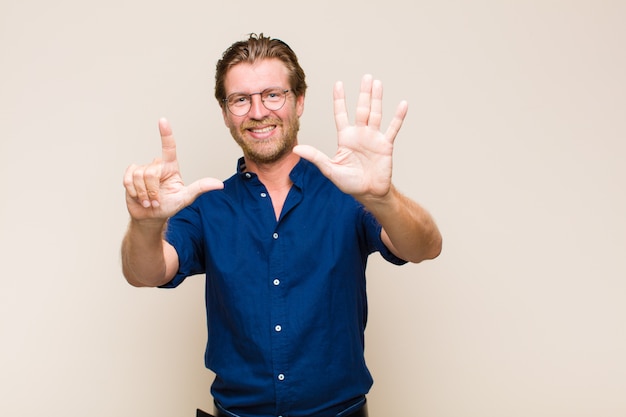 Blonder erwachsener Mann lächelt und sieht freundlich aus, zeigt Nummer sieben oder siebte mit der Hand nach vorne, Countdown