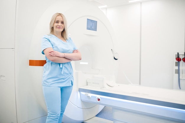 Blonder Facharzt in blauer Uniform in der Nähe des MRI-Scanners