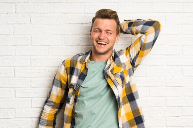 Blonder gutaussehender Mann über dem weißen Backsteinmauerlachen