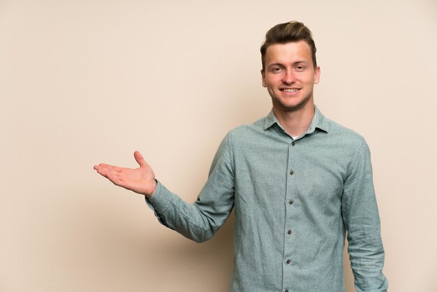 Foto blonder gutaussehender mann über lokalisierter wand, die copyspace eingebildet auf der palme hält