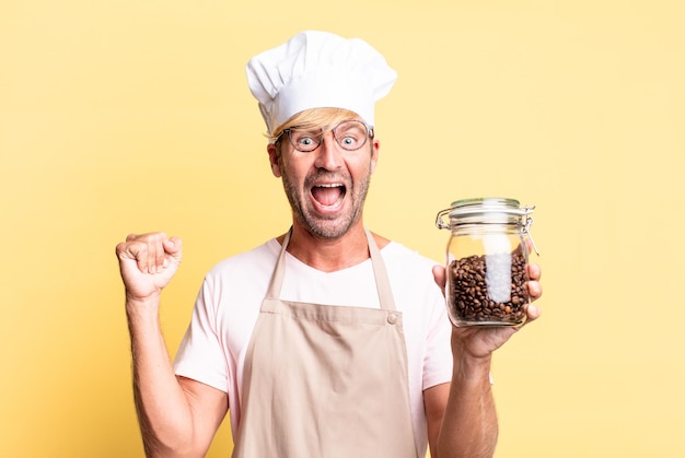 Blonder hübscher erwachsener Mann des Chefkochs, der eine Kaffeebohnenflasche hält