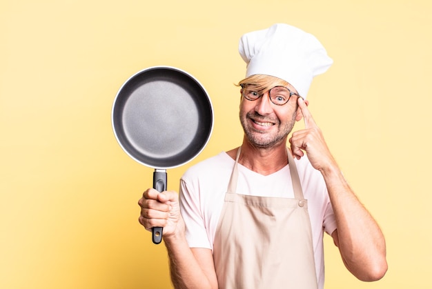 Blonder hübscher erwachsener Mann des Chefs, der eine Pfanne hält