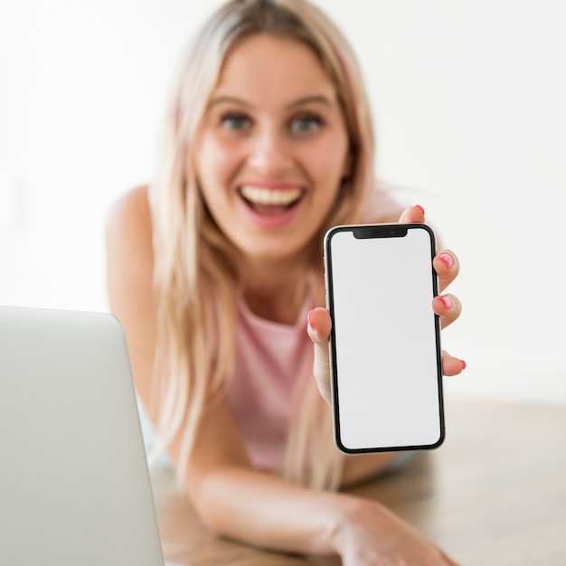 Blonder Influencer, der Smartphone auf dem Boden zeigt