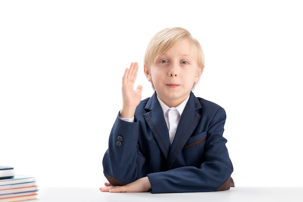 Blonder Junge in Schuluniform hob seine Hand hoch, um die Frage des Lehrers zu beantworten Portrait of knowitall boy Isolated on white Background