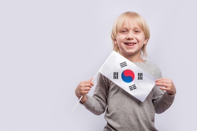 Blonder Junge lächelt und hält Flagge von Südkorea. Bildung in Korea.