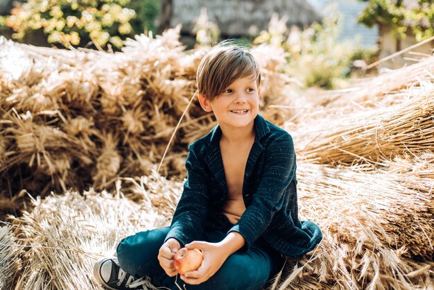 Blonder Junge liegt auf Heuhintergrund und isst einen Apfel. Sale für die gesamte Herbstkollektion, unglaubliche Rabatte und eine wunderbare Auswahl. Tschüss Sommer - hallo Herbst. Zurück zur Schule.