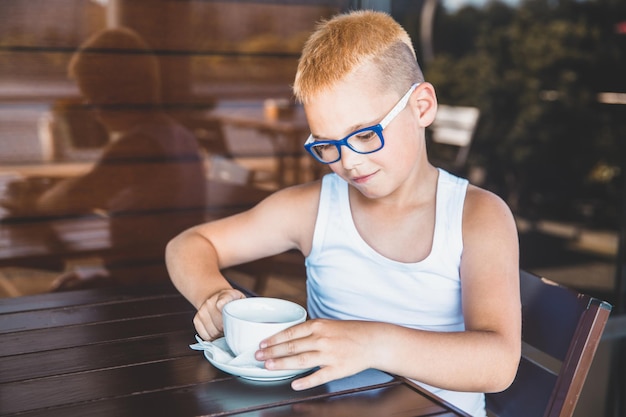 Blonder Junge mit Brille sitzt in einem Café und trinkt Kaffee