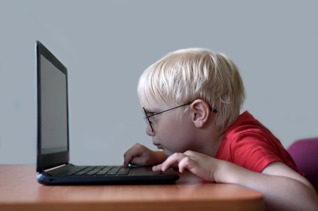 Blonder Junge mit Brille sitzt seine Nase in einem Laptop begraben. Internet und Vorschulkind